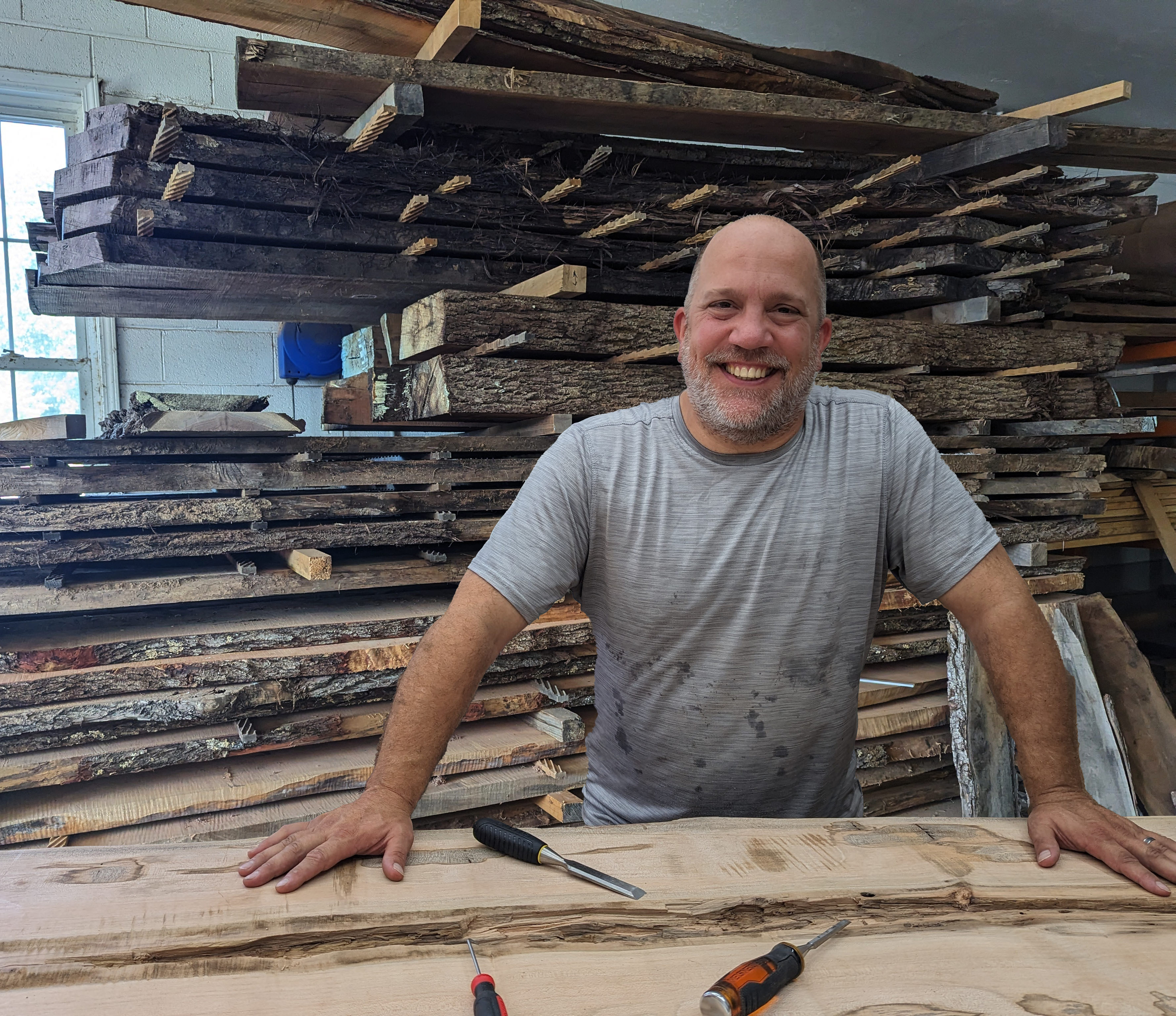 Owner Andy Peck leaning on his work bench in front of a wall of wood slats ready for prodction.