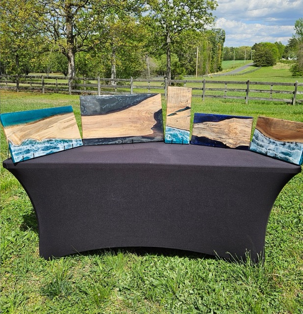A table sitting in a field with various cutting boards with epoxy detailing.