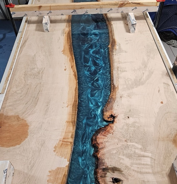 Photo of a table top being made. Two slabs of live edge wood with a river of blue epoxy in the center.