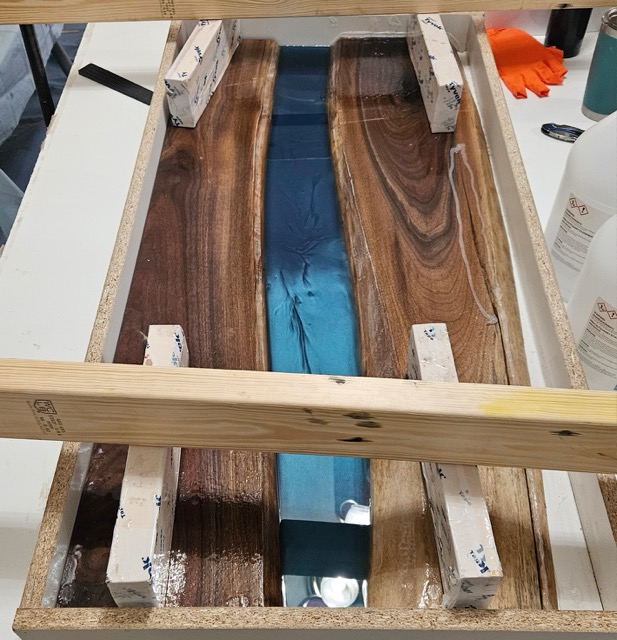 Two planks being held down by weights while a river of epoxy is hardening in the middle.