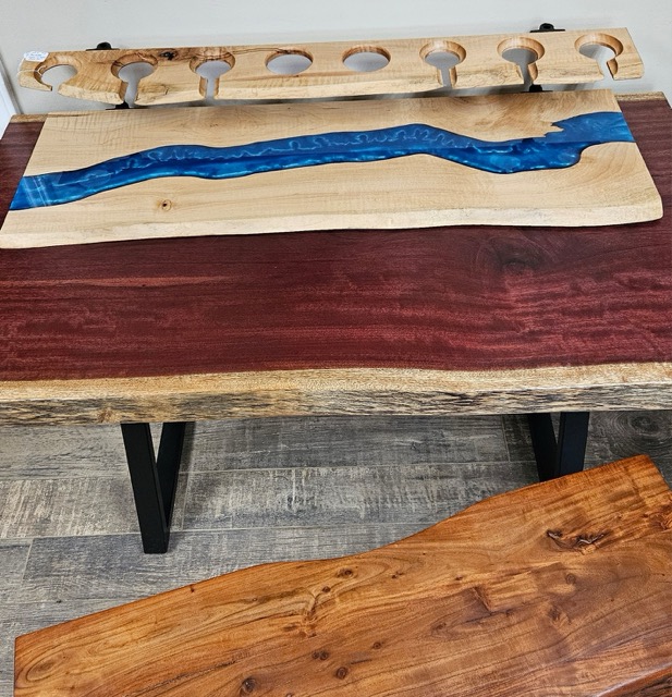 A wine bottle and wine glass holder with blue epoxy accents sitting atop a live edge table.