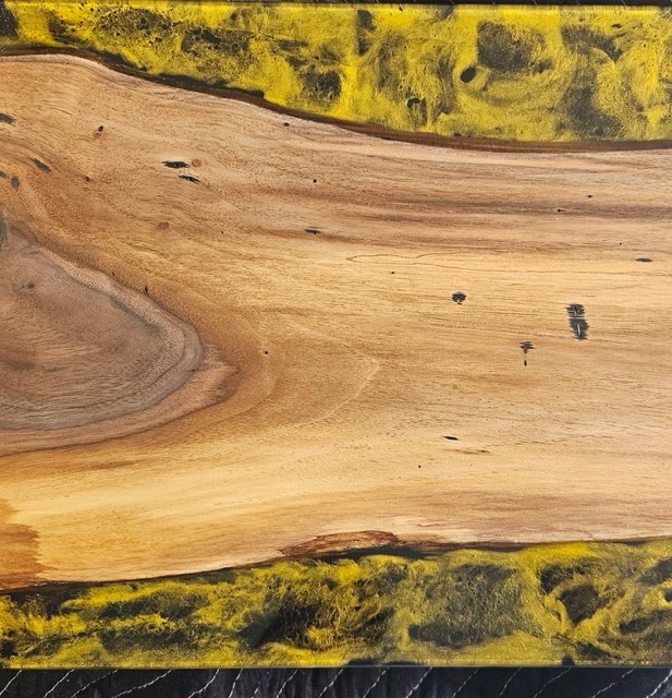 Close up of a live edge cutting board with a yellow and black epoxy on each edge.